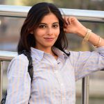 Portrait of a confident Indian woman standing outdoors, showcasing a casual elegance against a city backdrop.